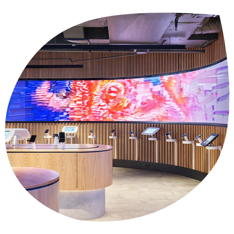 Image of an Optus store curved LED wall. Attached to the wall are a series of phones and ipads.