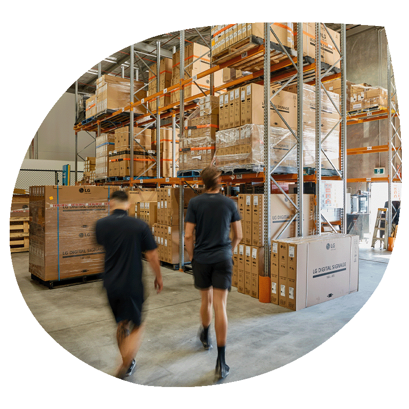Two workers in a warehouse walking towards a number of boxed on shelves.