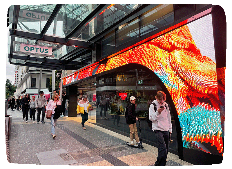 Outside of an Optus building with pedestrians walking past and a large LED screen wrapped around the front.