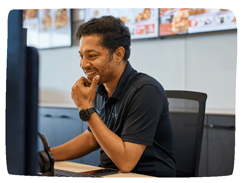 Entwined employee sitting at desk smiling while working on his computer.