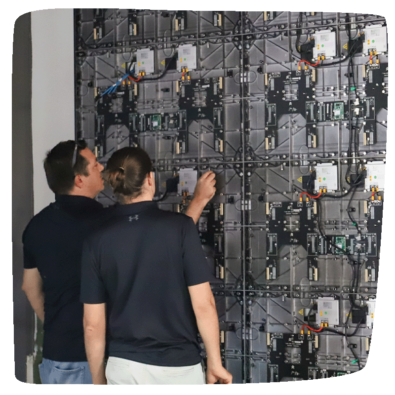 Two Entwined employees working on the backend of LED monitors against a wall.