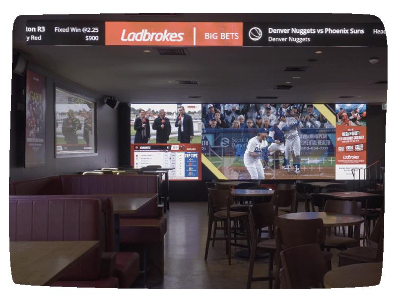 Inside a pub, looking at a back wall that has had a large digital screen installed on it, displaying sport content. 