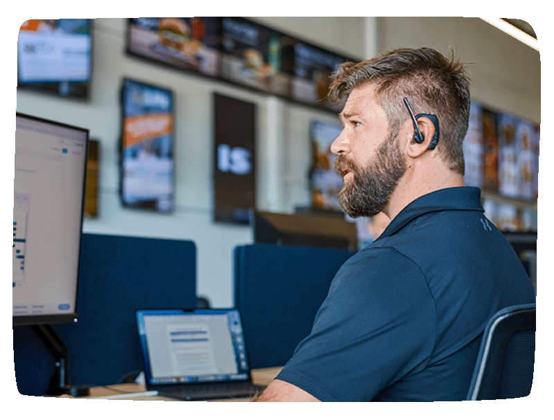 Man sitting at a desk working with a headset on his right ear. 