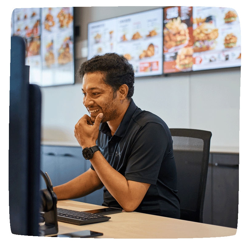 Support staff smile at computer with digital displays on the wall behind