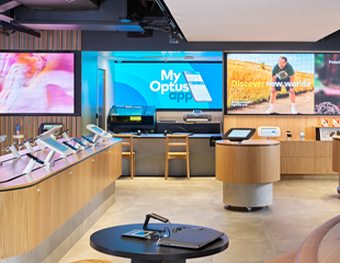 A look at the inside of an Optus shop with a wide variety of digital screen on the walls with tablets and phones showcased around the room.